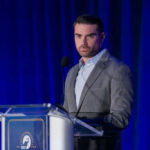 Man speaking at a podium with blue curtains