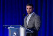 Man speaking at a podium with blue curtains