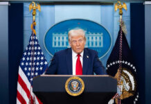 Man speaking at podium with flags in background