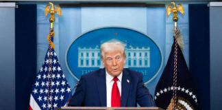 Man speaking at podium with flags in background