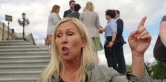 A woman passionately speaking outdoors, surrounded by people and media.