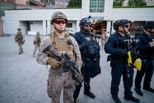 Military and police personnel in tactical gear standing in an urban area