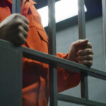 Person in orange jumpsuit behind jail bars