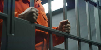 Person in orange jumpsuit behind jail bars