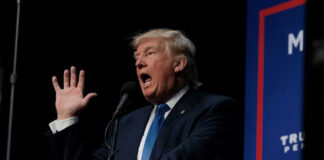 Man speaking at a podium with raised hand