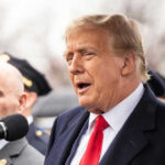Two men speaking at an outdoor event in suits