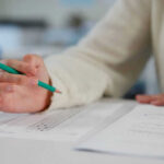 Person holding pencil over exam paper on table