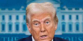 Person speaking wearing suit with American flag pin