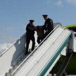 Police officers escorting a passenger down the stairs from an airplane