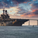 Aircraft carrier near bridge under colorful sunset sky