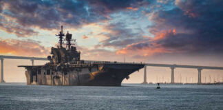 Aircraft carrier near bridge under colorful sunset sky