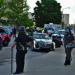 Police officers in riot gear managing a scene with emergency vehicles