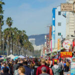 Crowded Venice Beach boardwalk with palm trees and shops