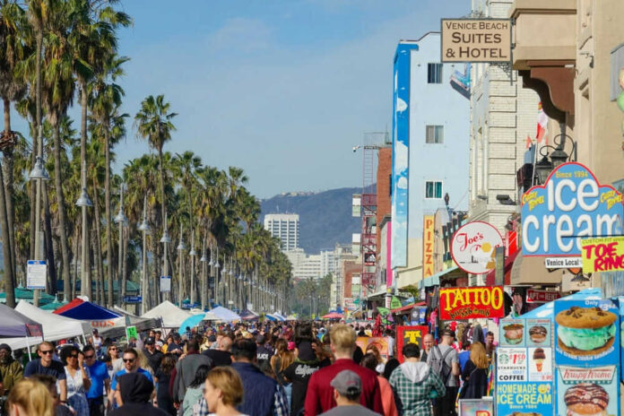 shutterstock_2474004039 Crowded Venice Beach boardwalk with palm trees and shops