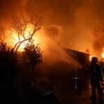 Firefighter battling blaze at night with hose spray