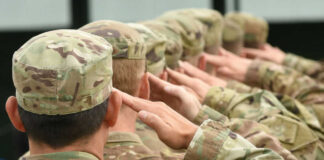 Soldiers saluting in camouflage uniforms with flag patches