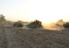 Military tanks moving through a dusty field at sunset