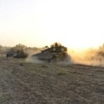 Military tanks moving through a dusty field at sunset